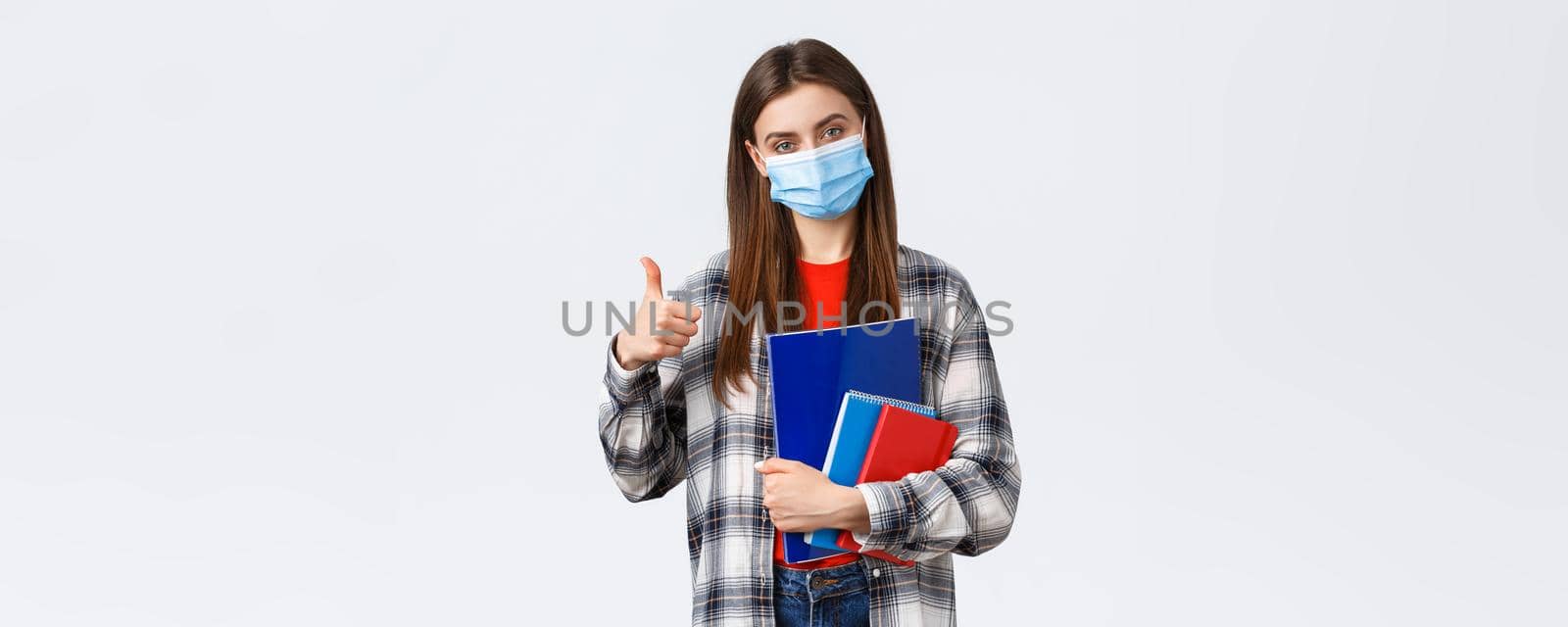 Coronavirus pandemic, covid-19 education, and back to school concept. Pleased young female freshman in college, showing thumb-up as studying prestige univeristy, carry notebooks.