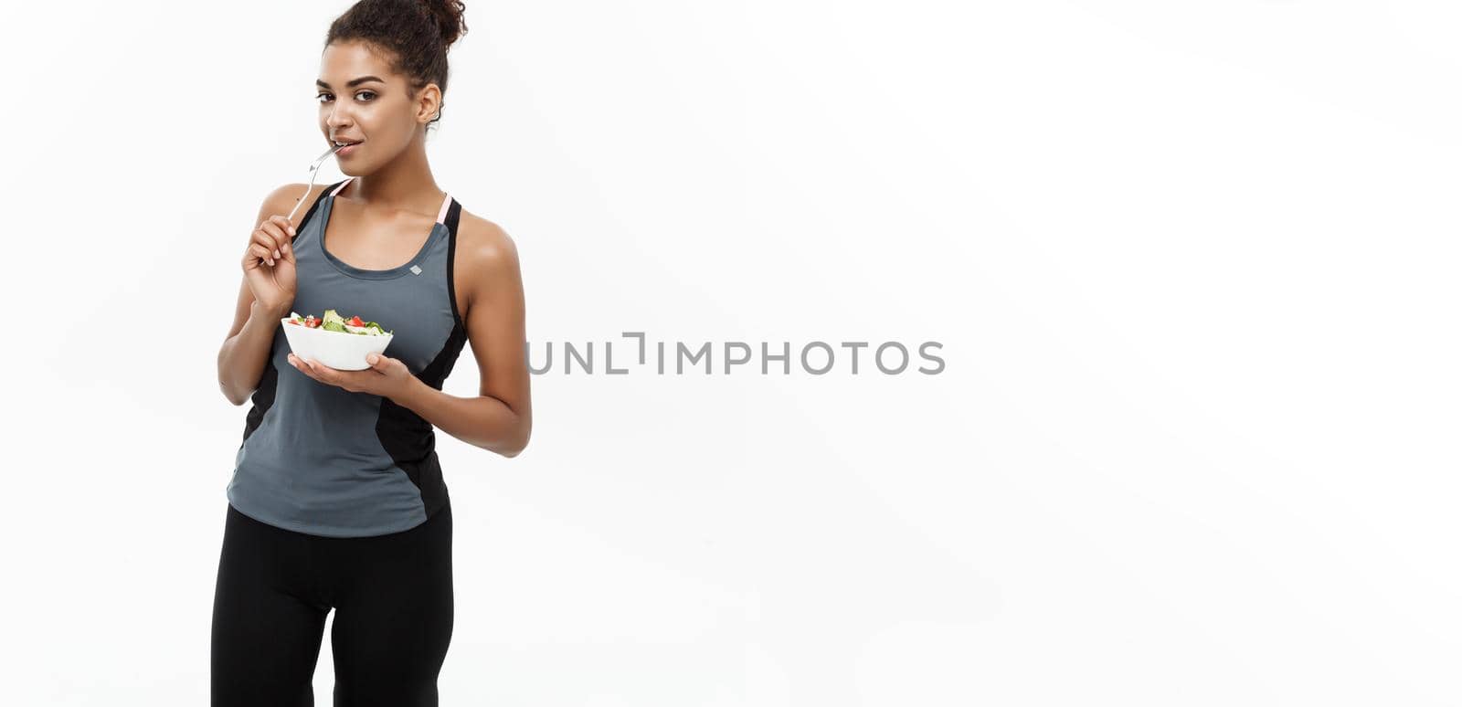 Healthy and Fitness concept - Beautiful American African lady in fitness clothes on diet eating fresh salad. Isolated on white background