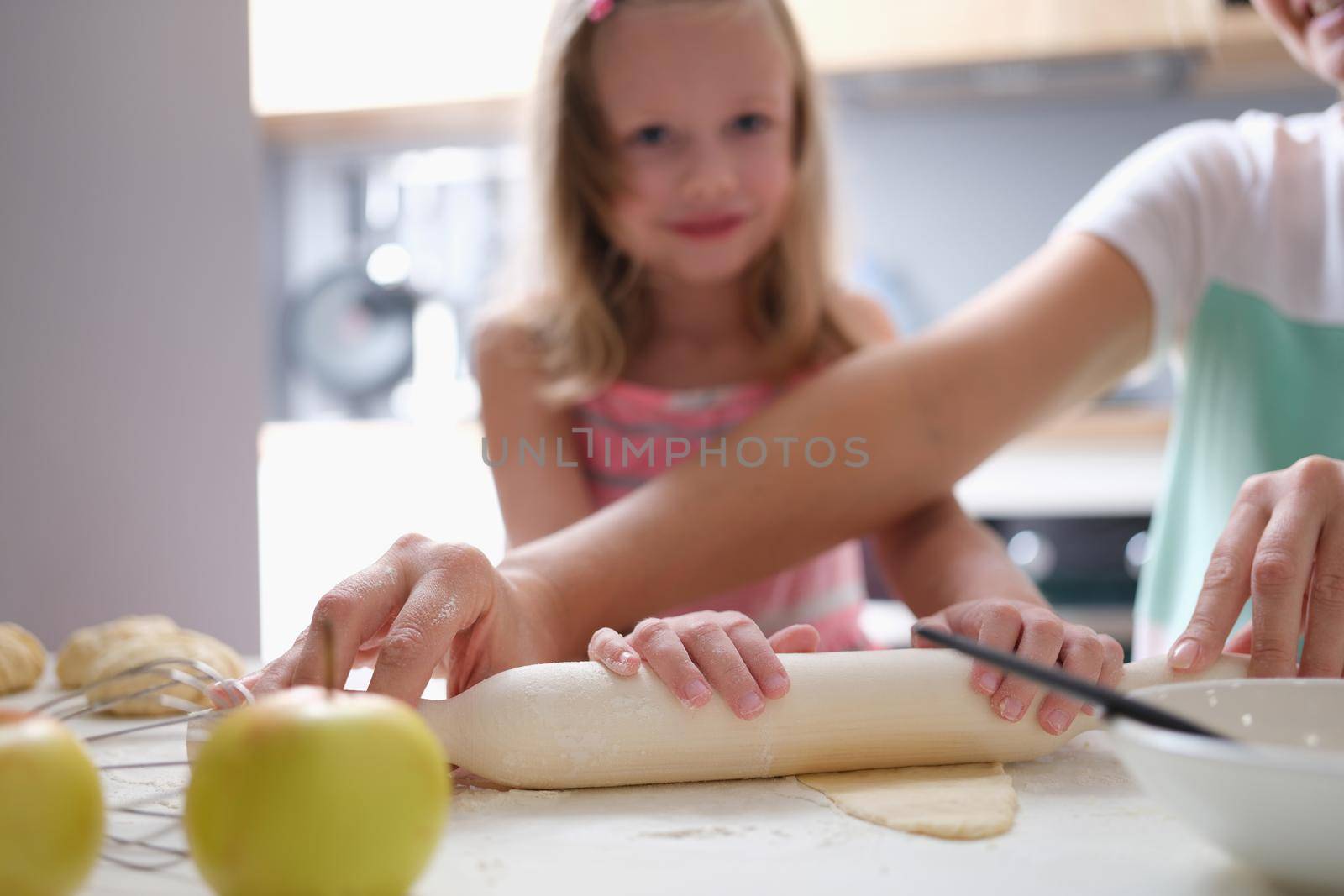 Mother and daughter roll out dough in kitchen at home closeup. Happy family cooking concept