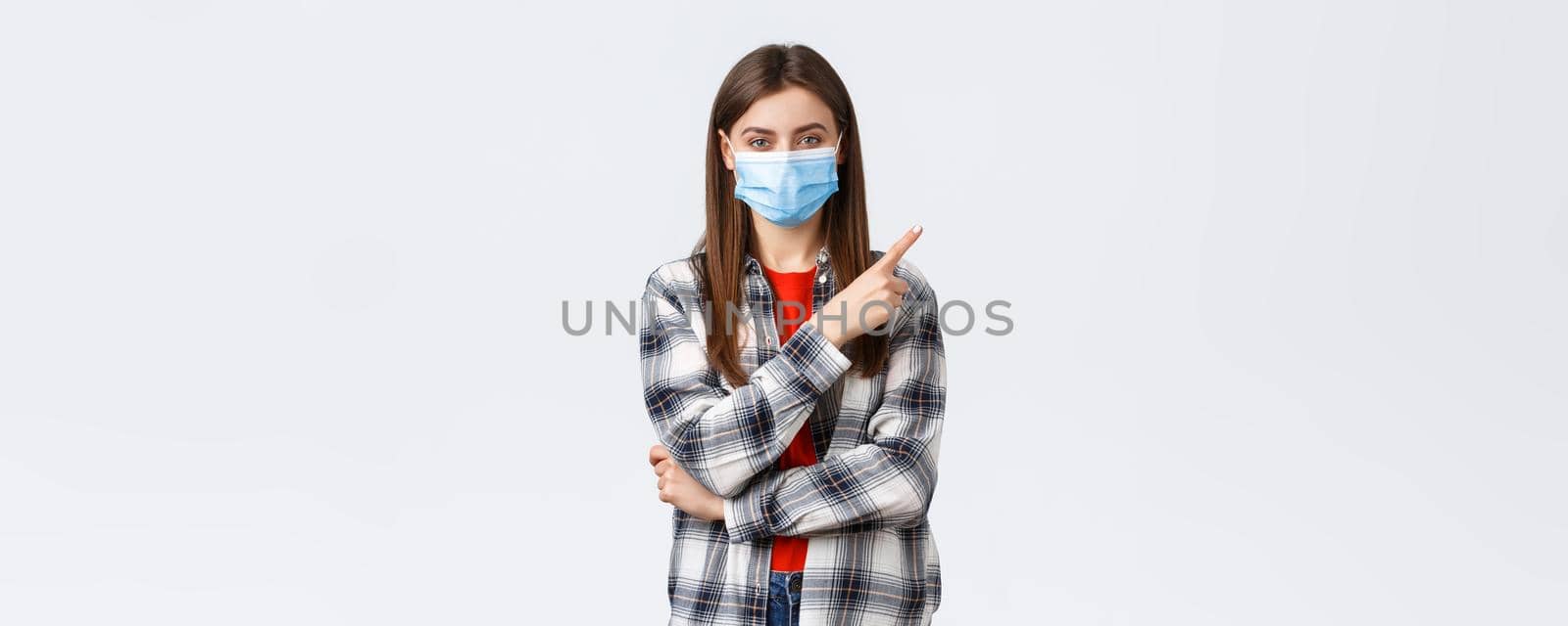 Coronavirus outbreak, leisure on quarantine, social distancing and emotions concept. Happy smiling young woman in medical mask provide information on covid-19 pointing finger upper right.