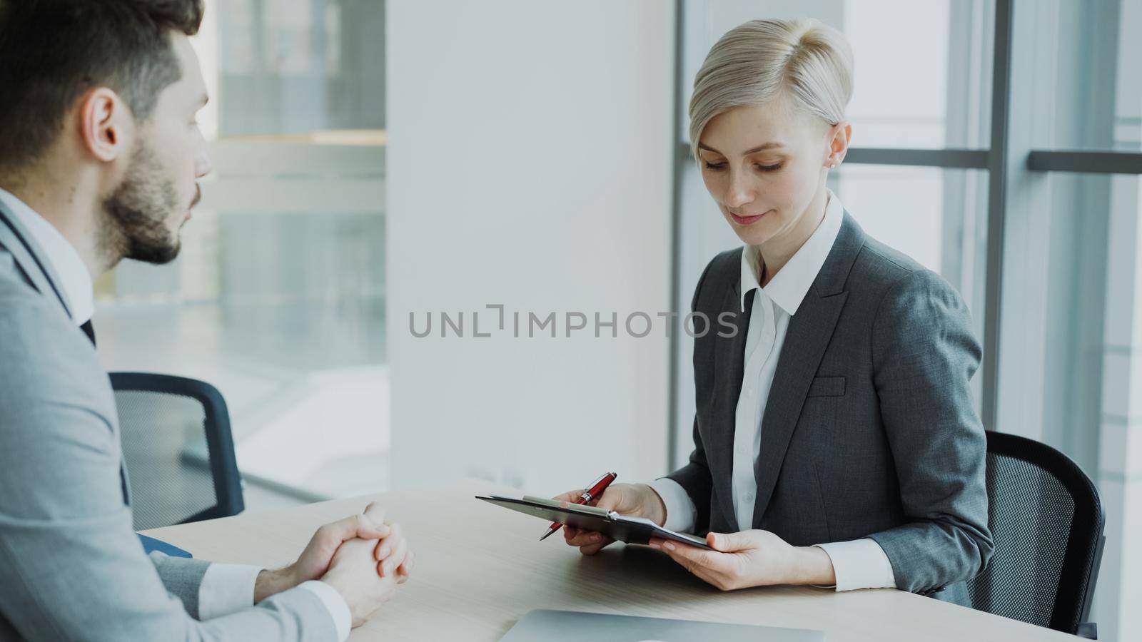 HR businesswoman having job interview with young man in suit and watching his resume application in modern office by silverkblack