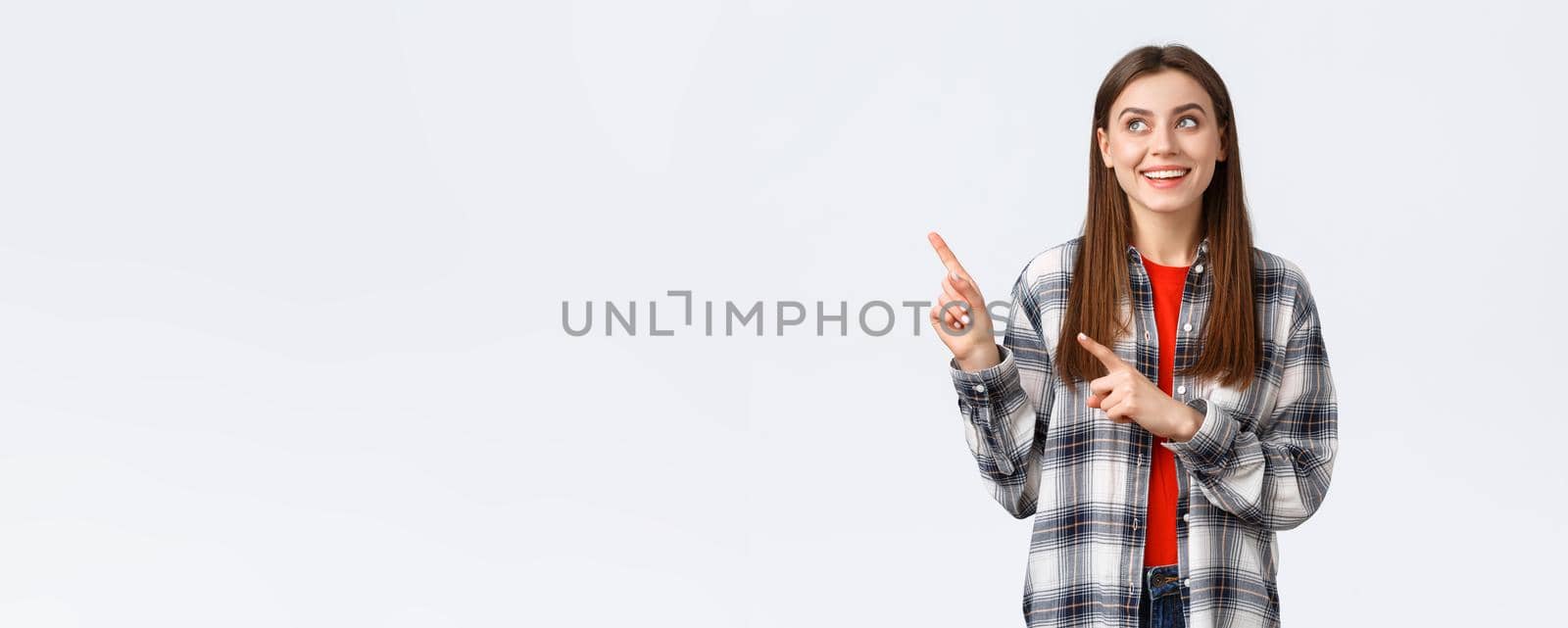 Lifestyle, different emotions, leisure activities concept. Dreamy cute smiling woman in checked shirt, pointing and looking upper left corner at best variant, picked or booked smth online by Benzoix