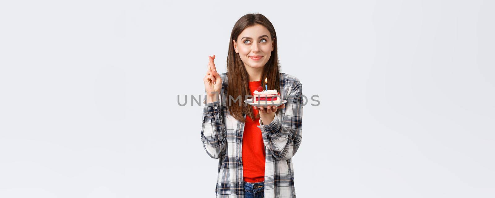 People lifestyle, holidays and celebration, emotions concept. Dreamy hopeful birthday girl in casual clothes, cross fingers and look up making wish, holding b-day cake, blowing candle.