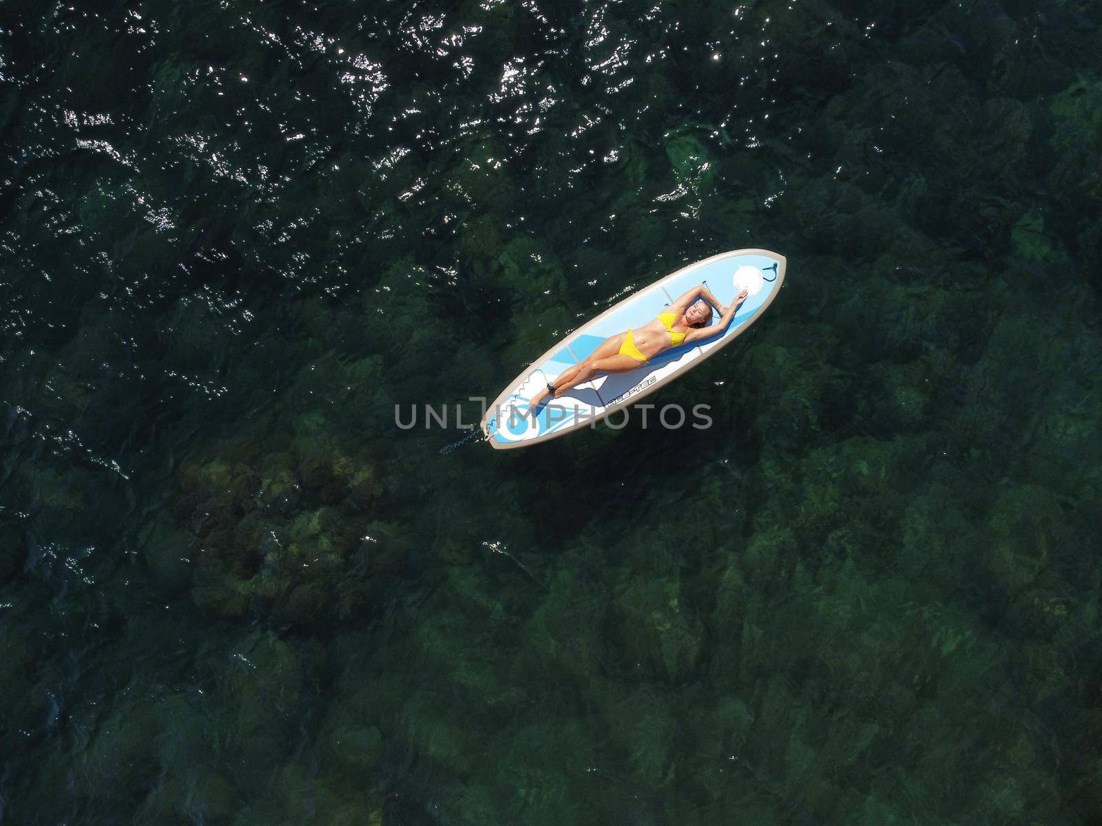 Side view foto of a woman sitting and relaxing on the sup board. Young attractive woman in the sea on the Stand Up Paddle Board SUP. The concept of an active and healthy life in harmony with nature.