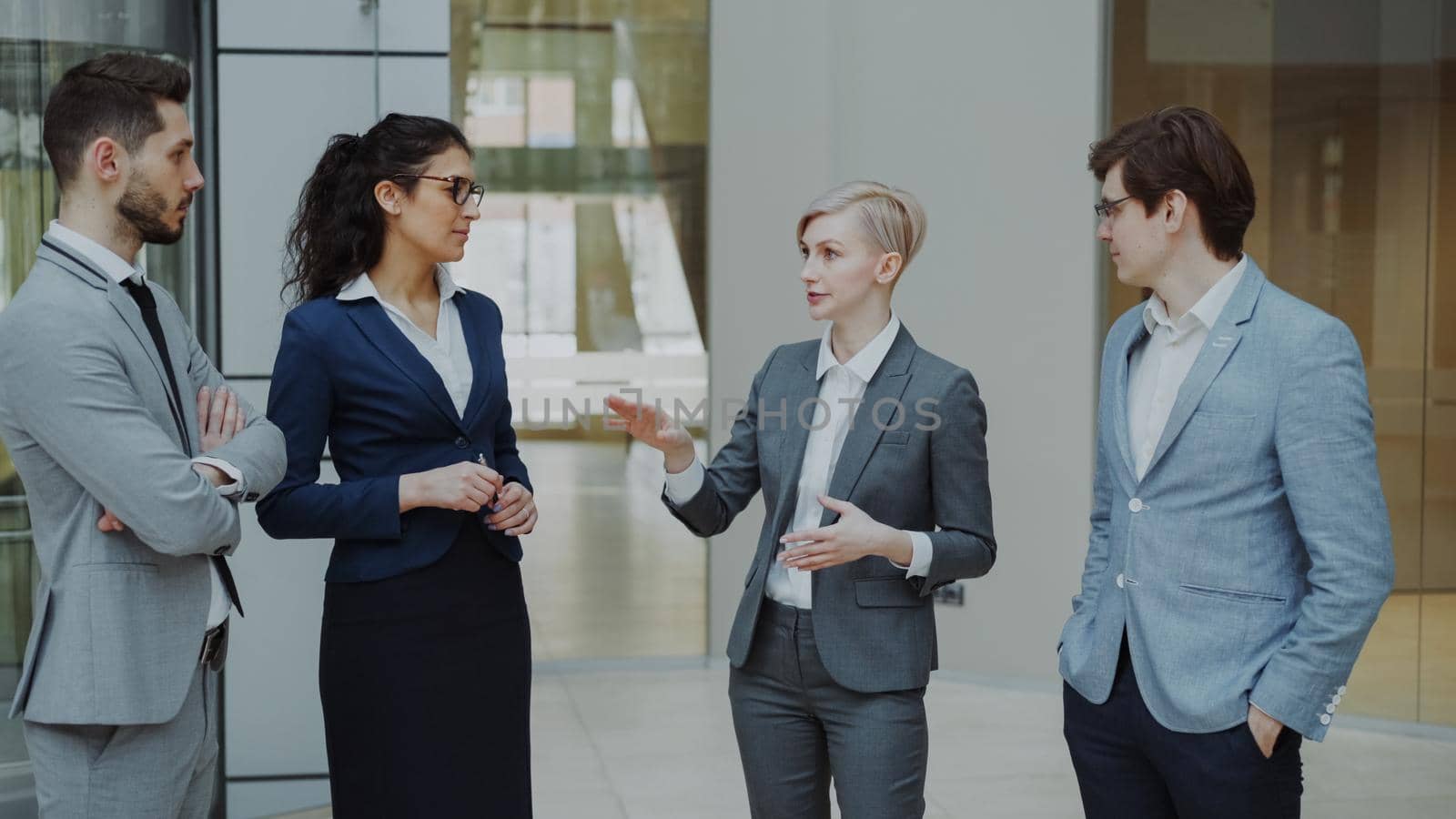 Businesswoman talking to her colleagues while standing in office lobby indoors. Group of business people discussing future deal