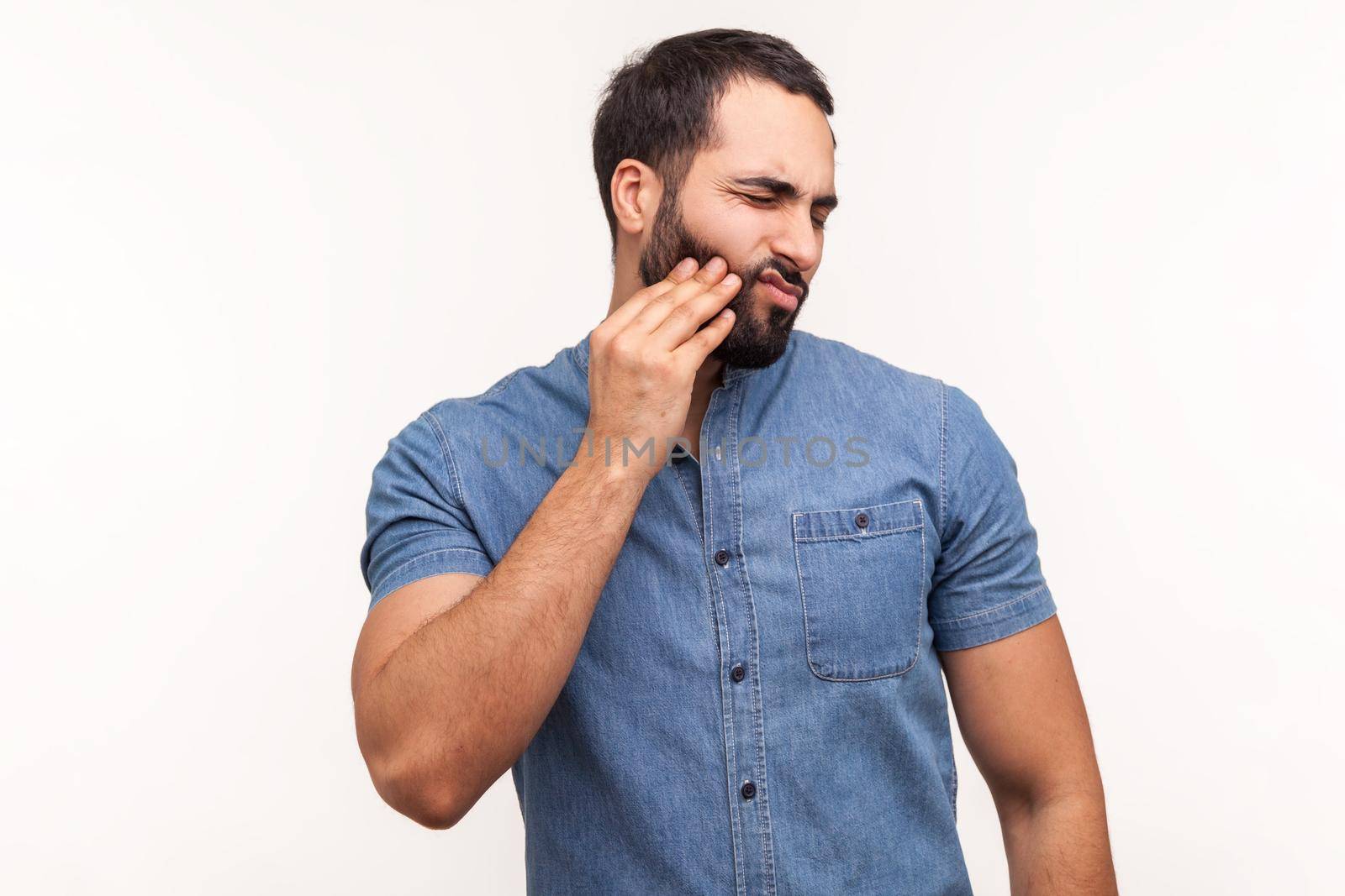 Sad unhappy man touching cheek feeling tooth pain and gums inflammation, oral cavity problems, need dentist consultation. Indoor studio shot isolated on white background