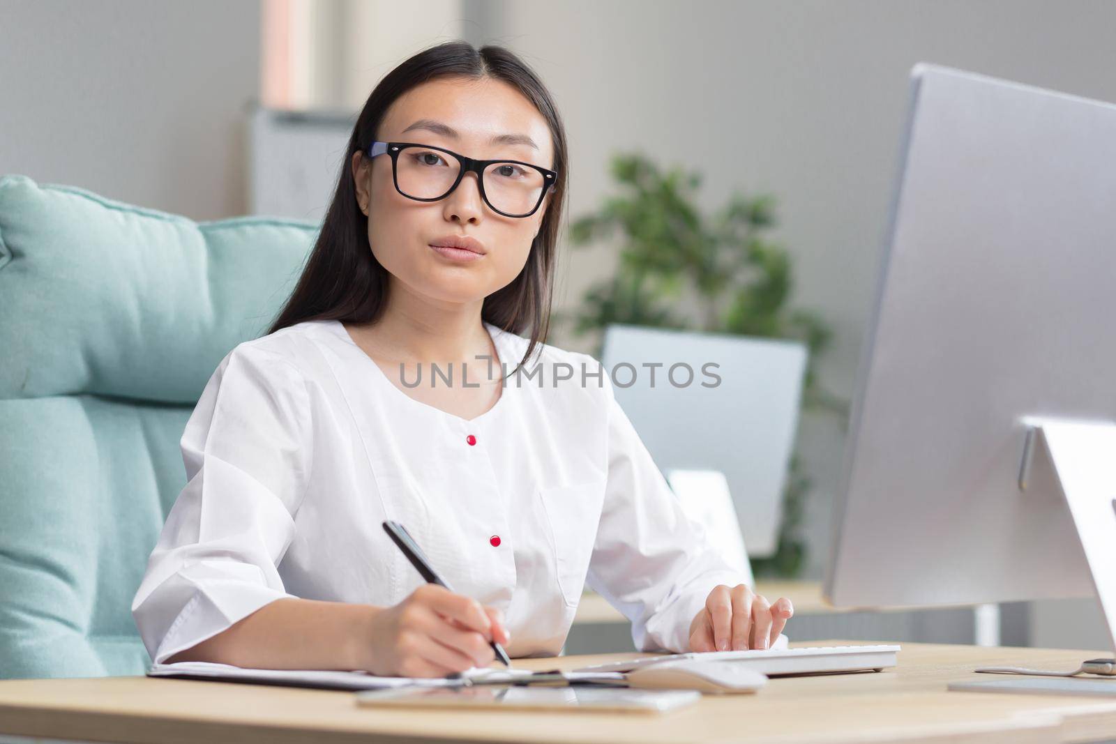 Portrait of young Asian female doctor, nurse woman looking at camera, working in office on paper work by voronaman