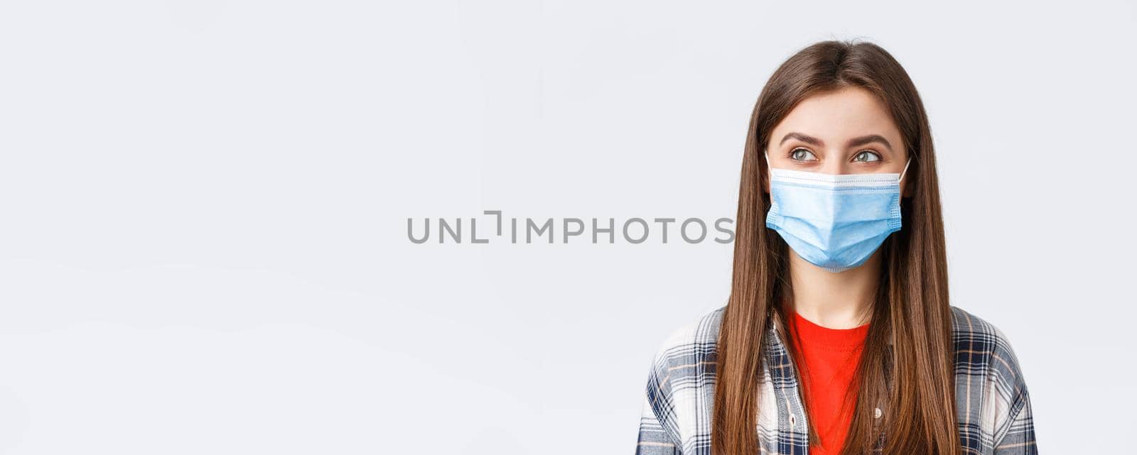 Coronavirus outbreak, leisure on quarantine, social distancing and emotions concept. Close-up of pleased cute girl smiling in medical mask, looking left at pleasant good thing, white background.