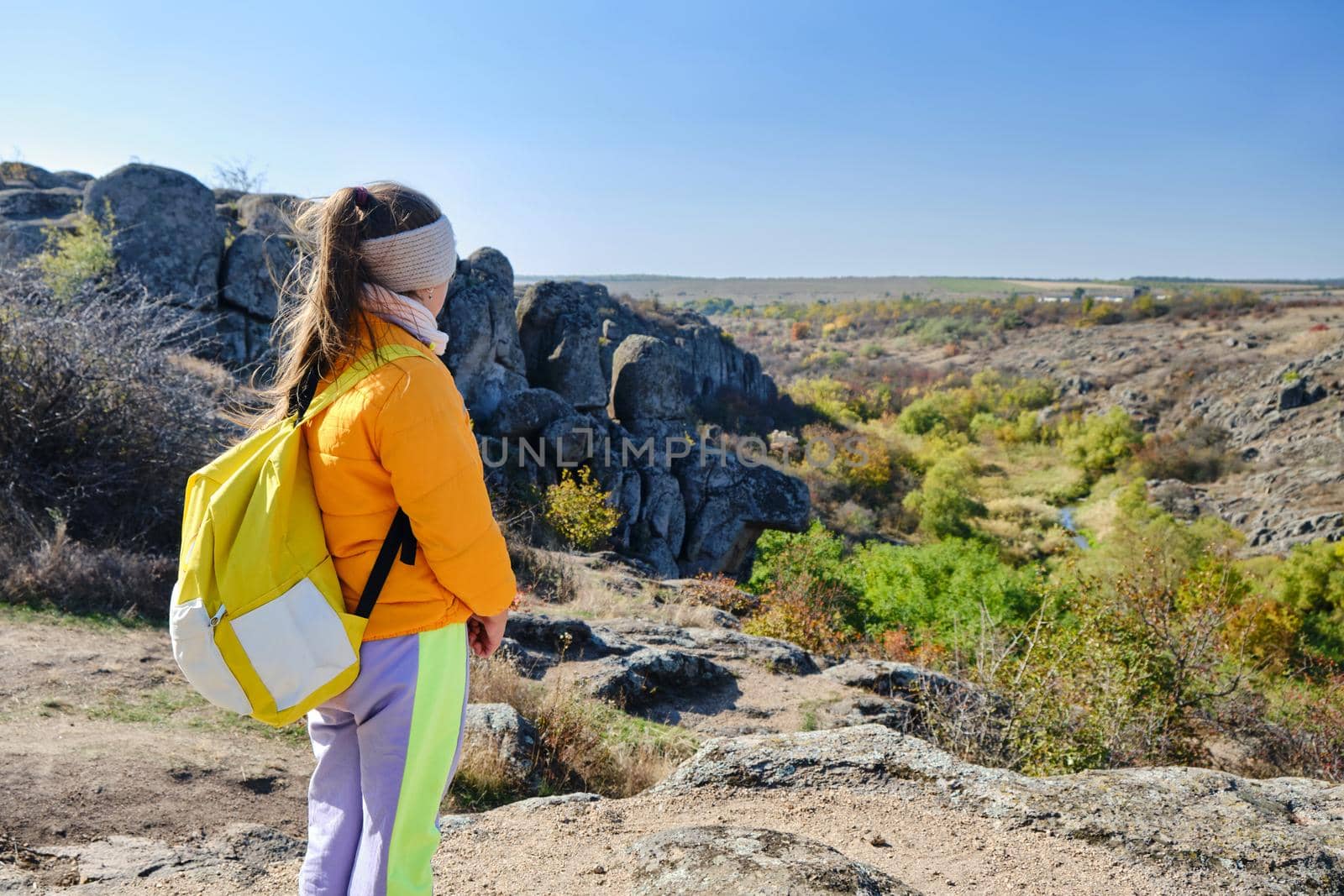 little girl with a yellow backpack standing on a mountain top at the day time