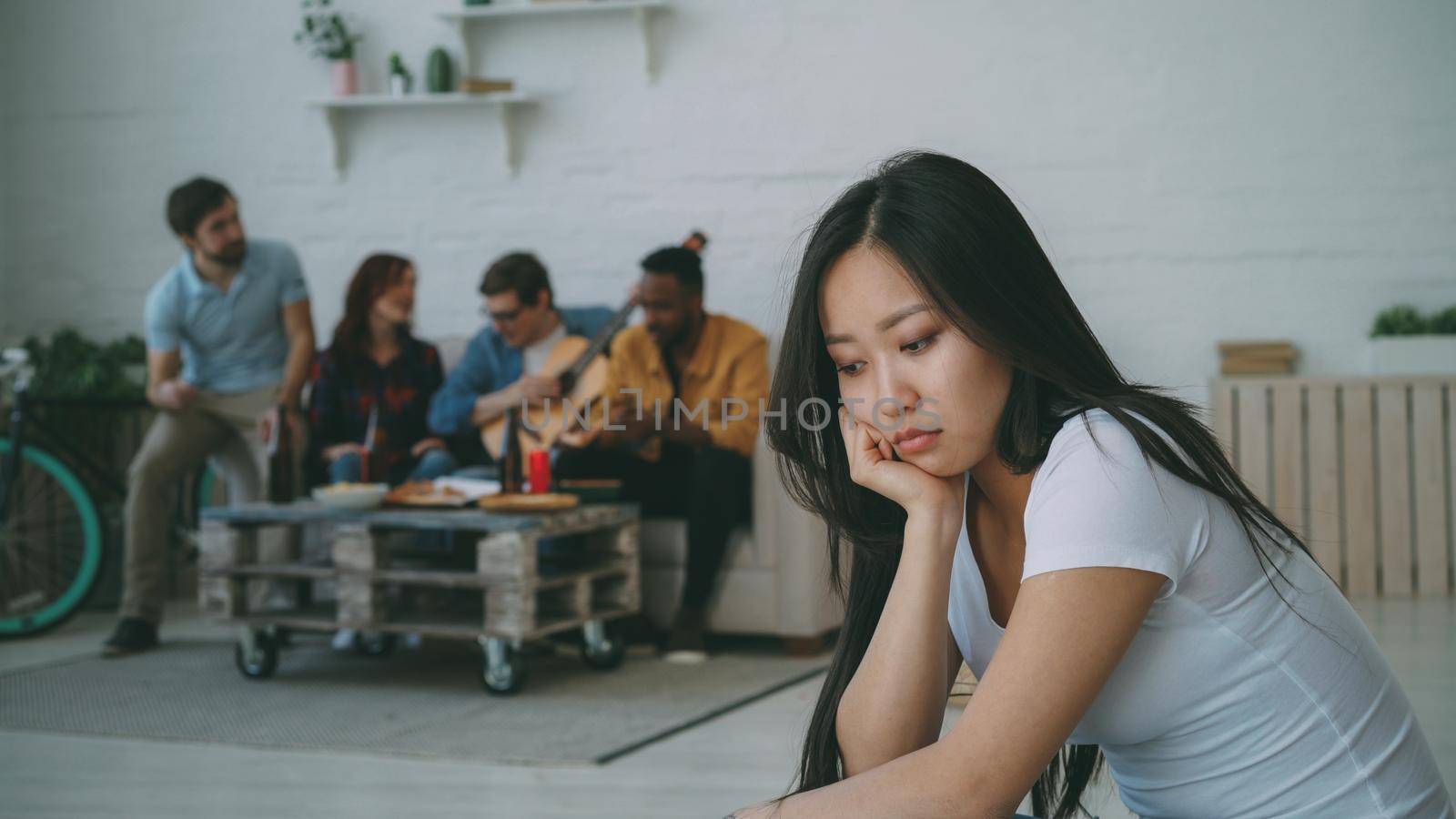 Young asian girl feels upset and isolated while her flatmates celebrating party at home indoors by silverkblack