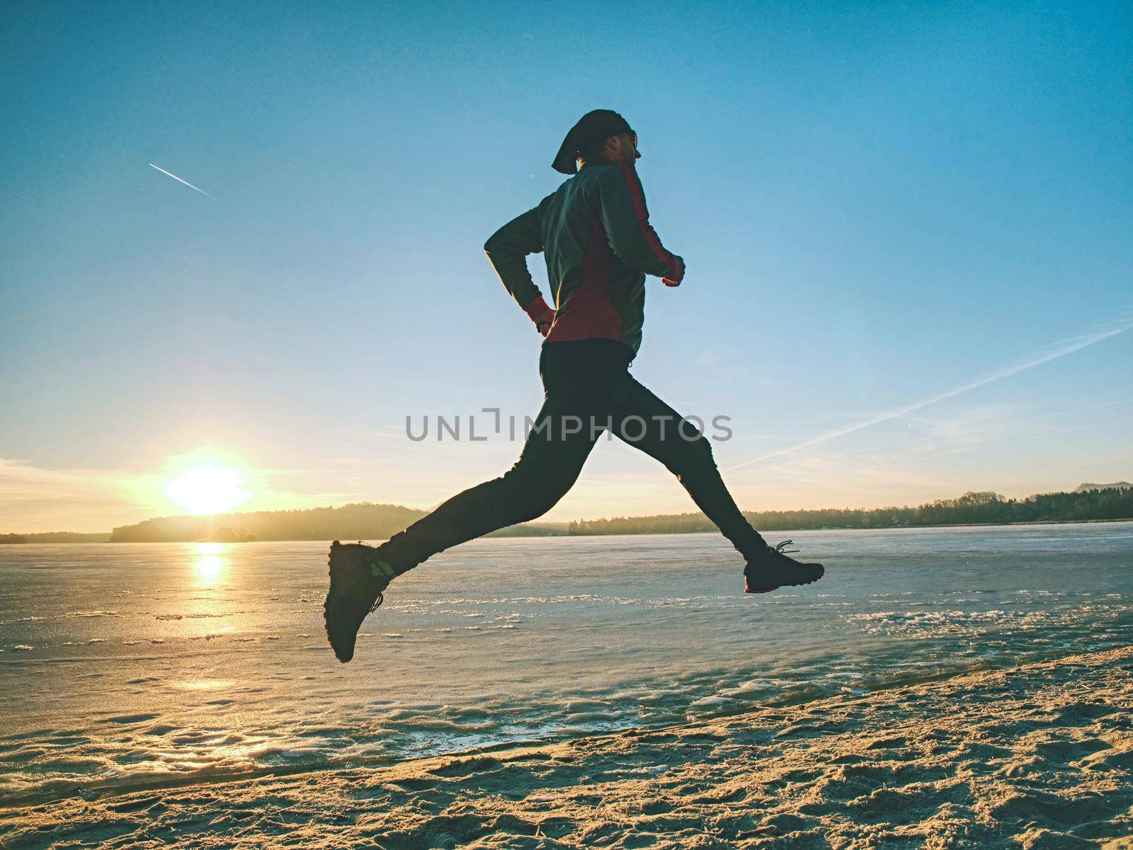 Fitness, sport, people, winter season and healthy concept - man running along ice covered winter river