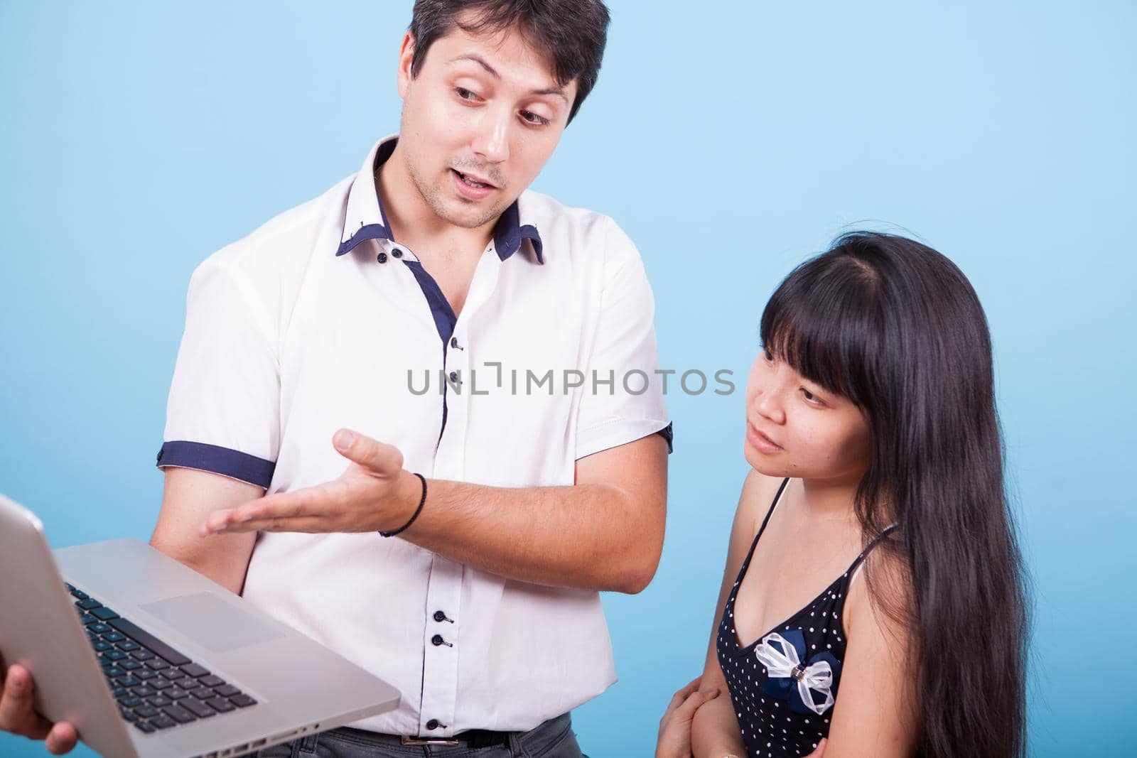 Cacausian male showing his asian girlfriend something on his computer in studio. Caucasian male married with asian female.