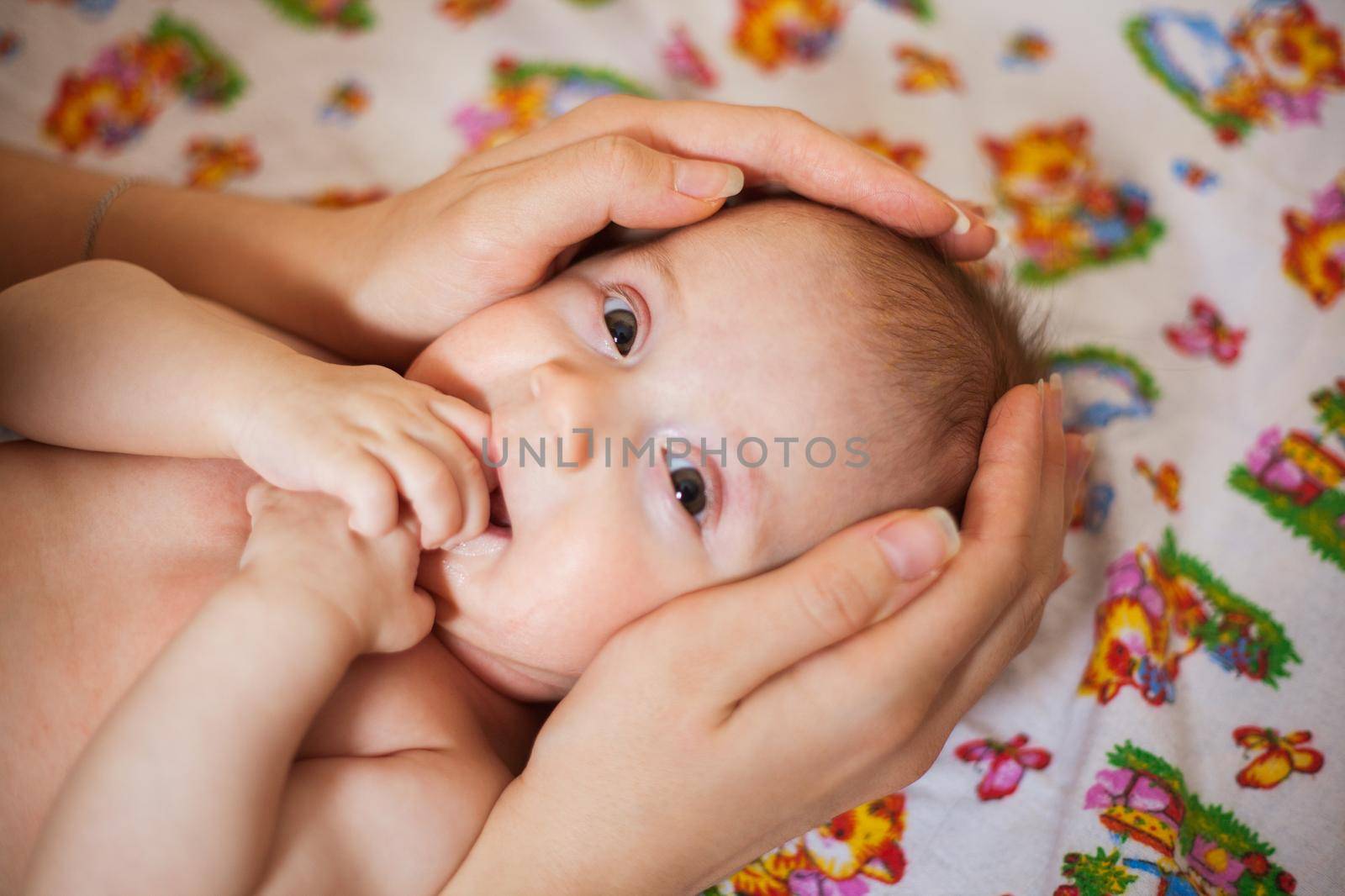 Mother holding head of her newborn daugther in hands. The baby on hands at mum. Loving mother hand holding cute smiling newborn baby child