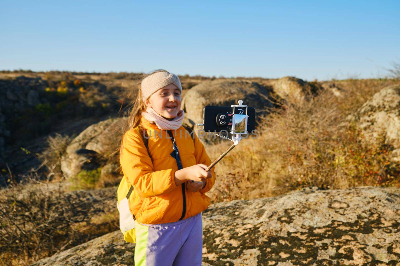 Shot of a kid girl talking on camera in hills, make video blog use device make video hold hand social network blog. child vlogger filming video diary outdoors. kid creating social media content.