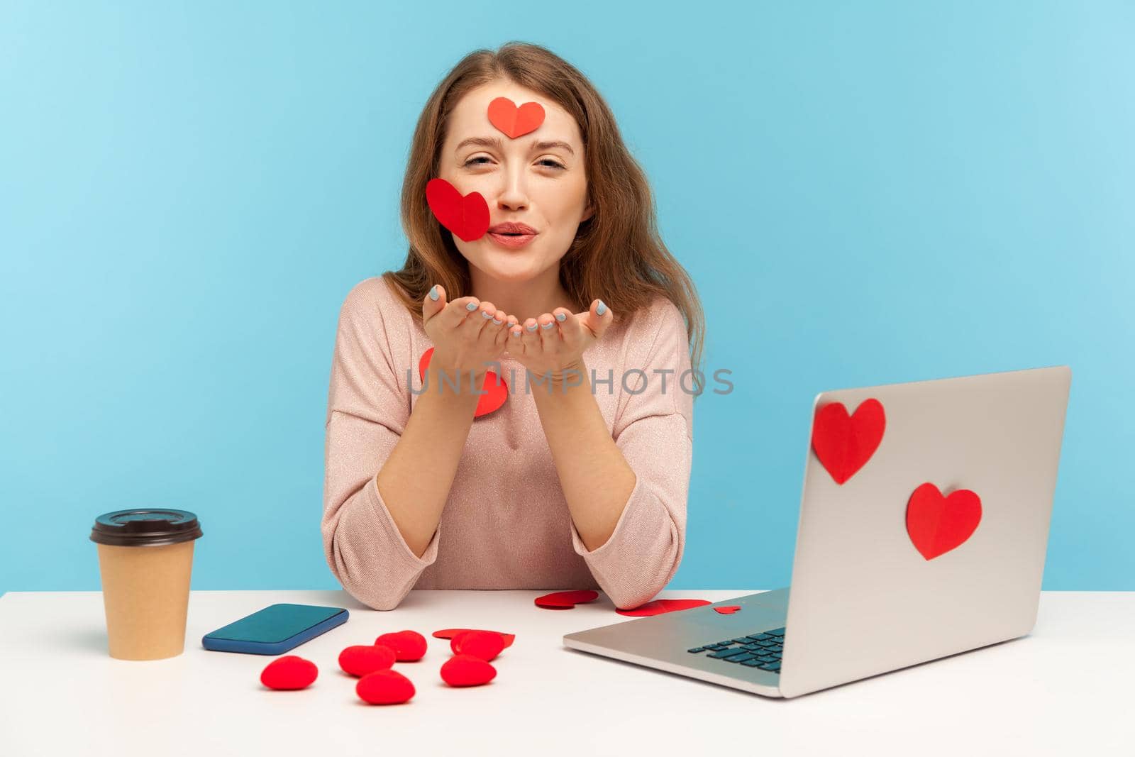 Love you. Amazing woman with kind expression sitting at workplace office, all covered with sticker hearts, sending romantic sensual air kiss, expressing romantic feelings. indoor studio shot isolated