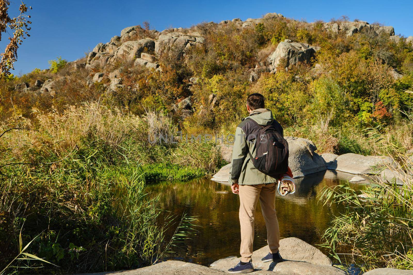 Hiker young man with backpack and trekking poles standing on edge of cliff and looking at the mountains in summer outdoor