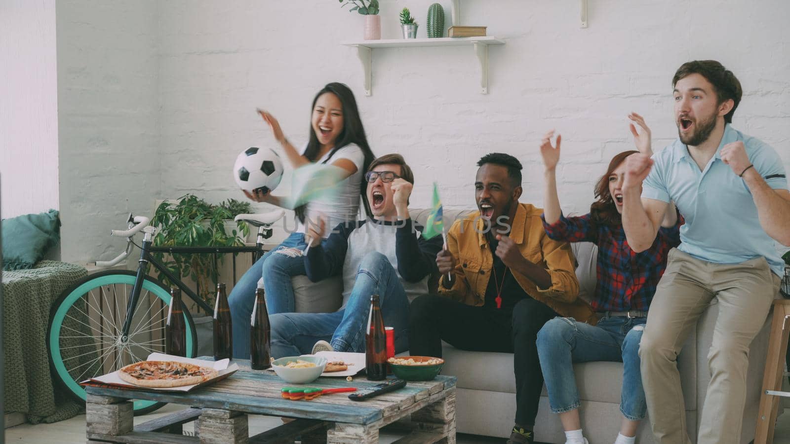 Multi-ethnic group of friends sports fans with Brazilian flags watching football championship on TV together at home and cheering up favourite team by silverkblack
