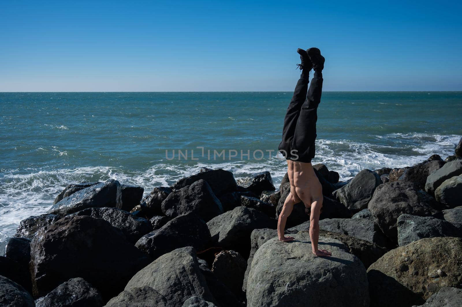 Shirtless man doing handstand on rocks by the sea