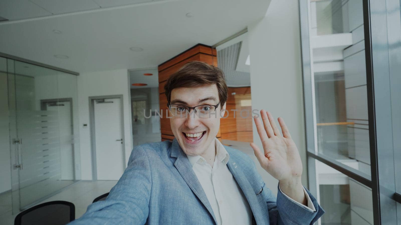 POV of young businessman in suit having online video chat using smartphone camera and talking to his colleagues in modern office by silverkblack