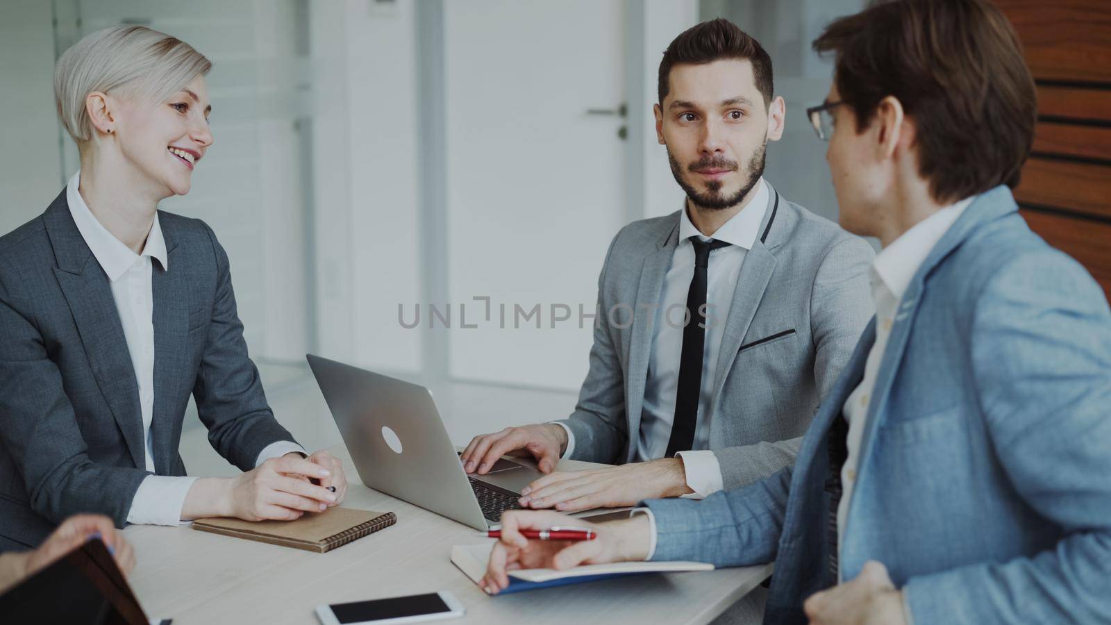 Businessman discussing future business project with male and female colleagues sitting at the table in modern office indoors