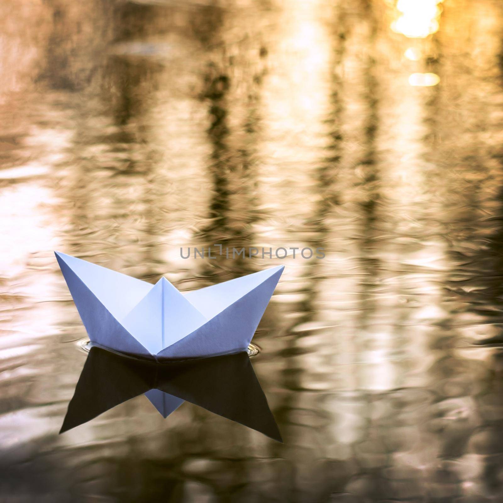 Small paper boat sailing down the river in Autumn at sunset