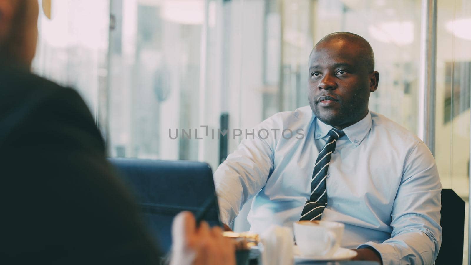 African American businessman explaining his startup details to investor in formal wear in glassy cafe during lunch time by silverkblack