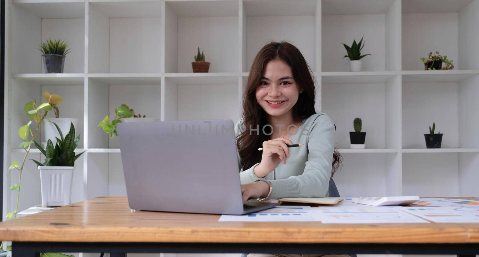 Portrait of an Asian young business Female working on a laptop computer in her workstation.Business people employee freelance online report marketing e-commerce telemarketing concept. by wichayada