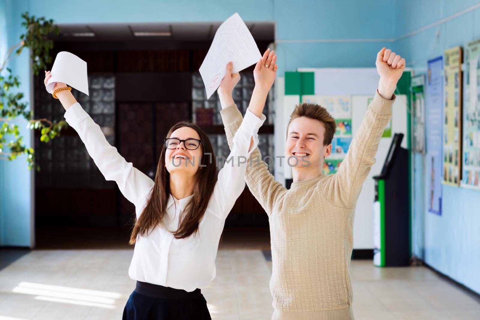 Happy students after researching their checked exams, raising hands up and expressing amusement of getting excellent grades for their work