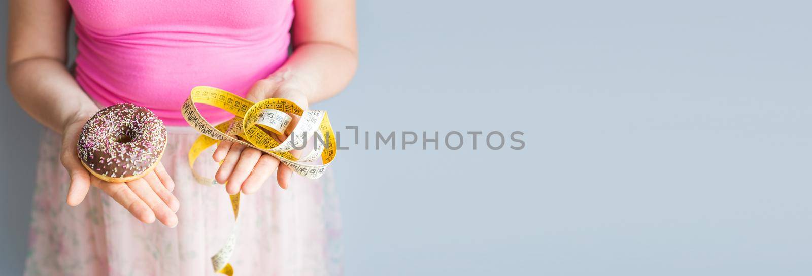 Close-up of woman's hands holding a donut and a measuring tape. The concept of healthy eating. Diet