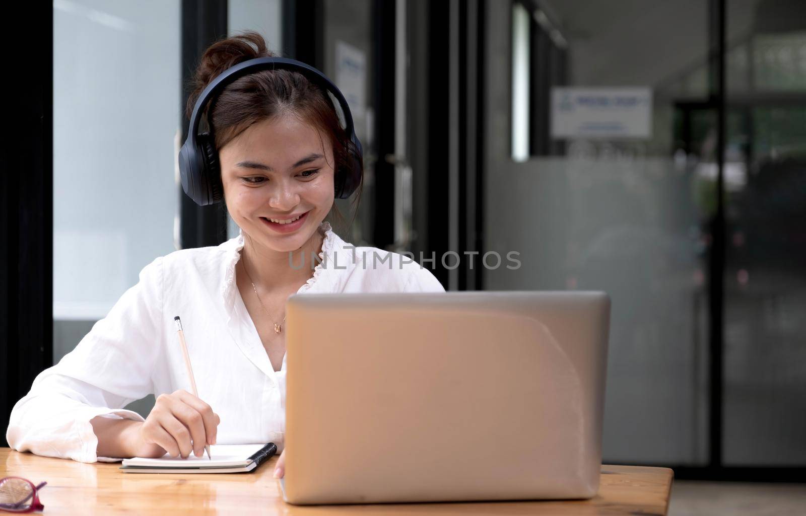 Young woman having online training, using laptop and wireless headset by wichayada