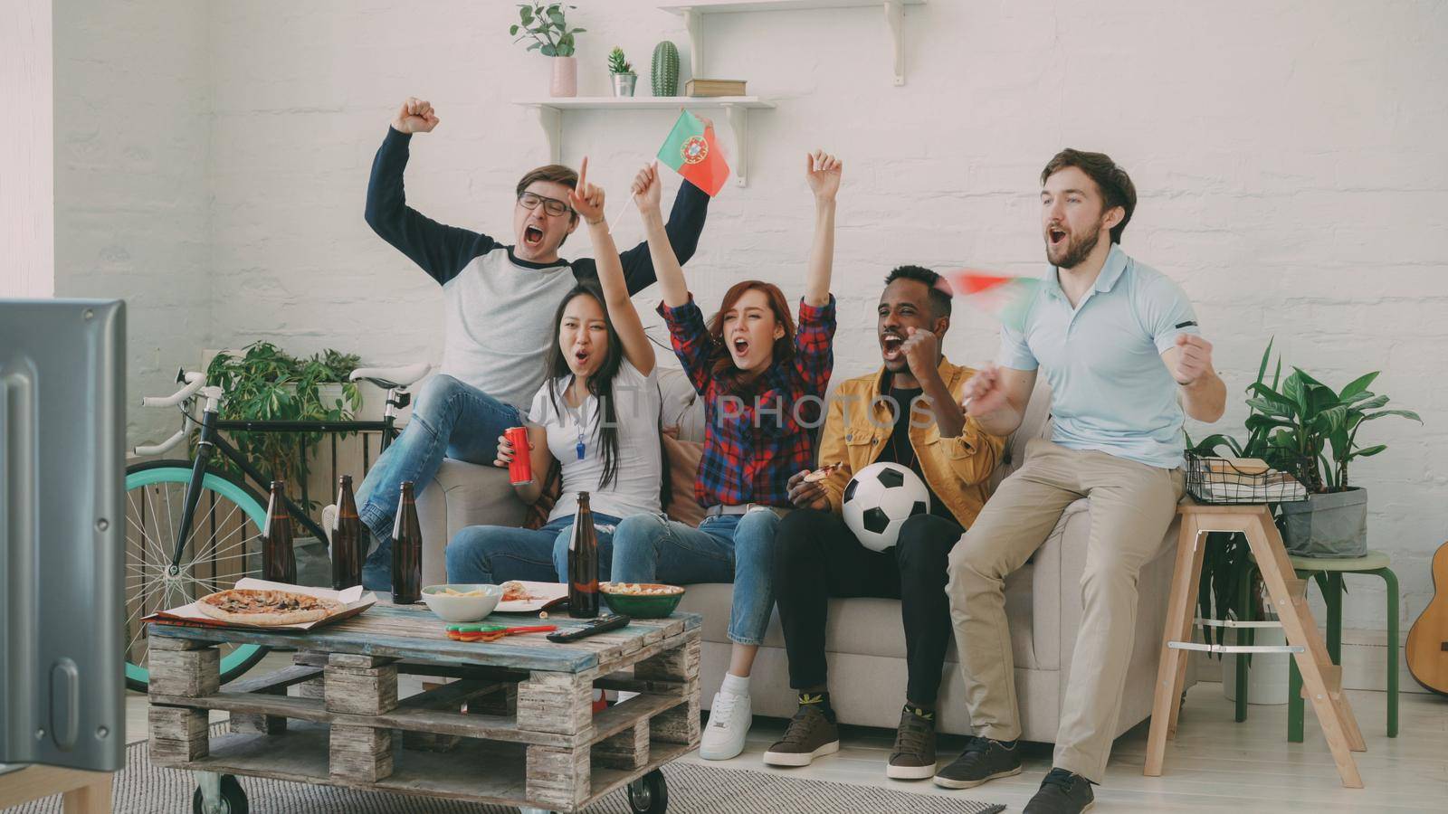 Happy friends with Portuguese flags watching sports championship on TV together at home indoors and happy about winning of favourite team