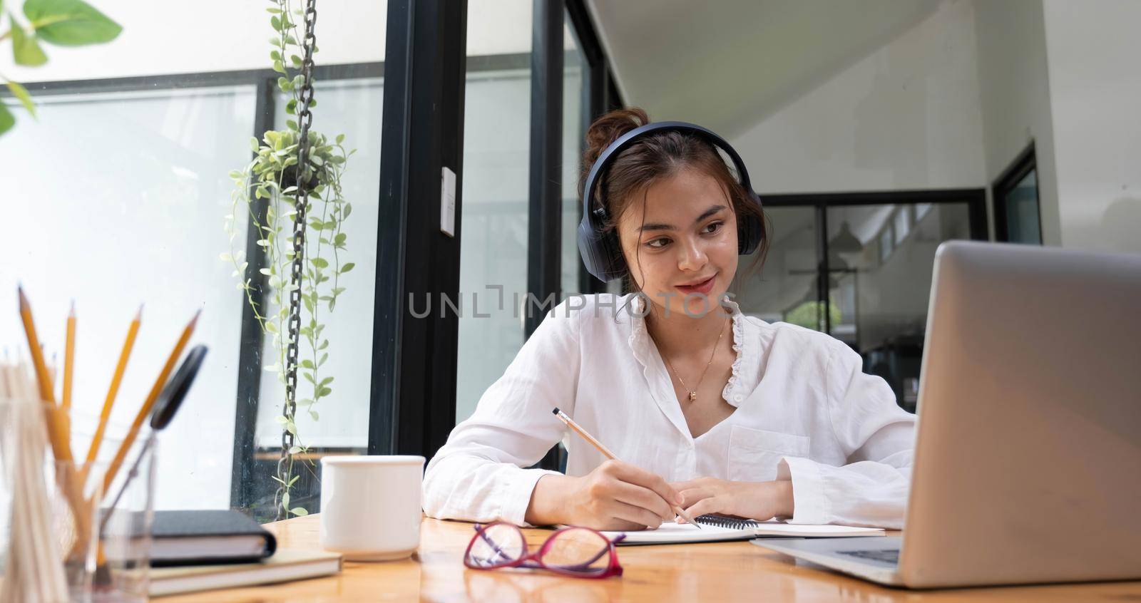 Smiling girl in headphones sit at desk look at laptop screen study online, happy smart young woman in earphones take web course or training on computer, distant education concept by wichayada