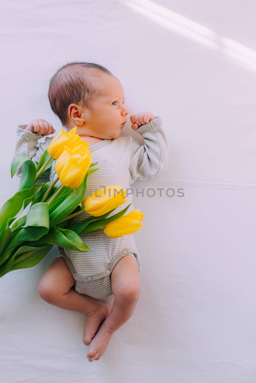 A newborn baby with a bouquet of tulips . A greeting card. March 8th. Baby and flowers. Yellow tulips
