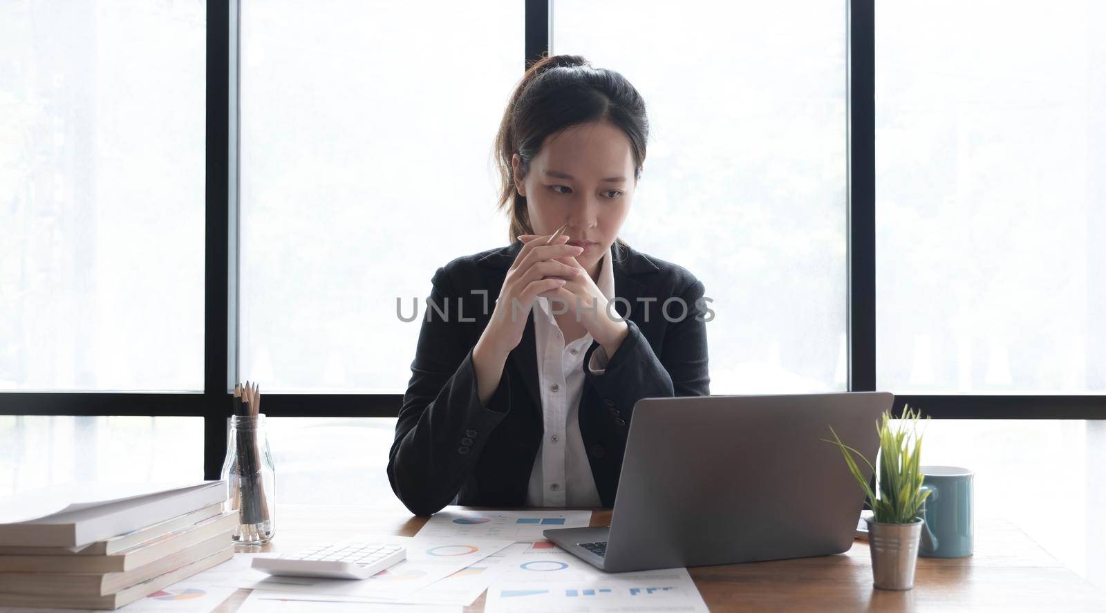 Image of an Asian woman who is tired and overthinking from working with a tablet at the office. by wichayada