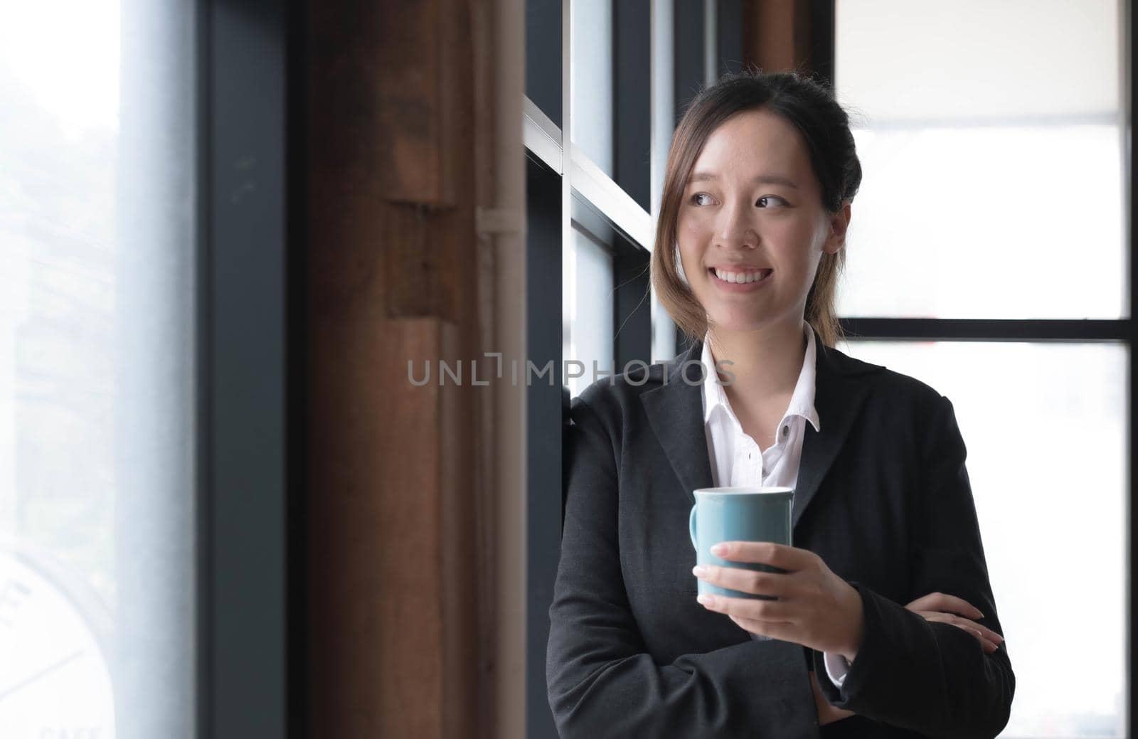 Smiling young Asian businesswoman holding a coffee mug at the office.