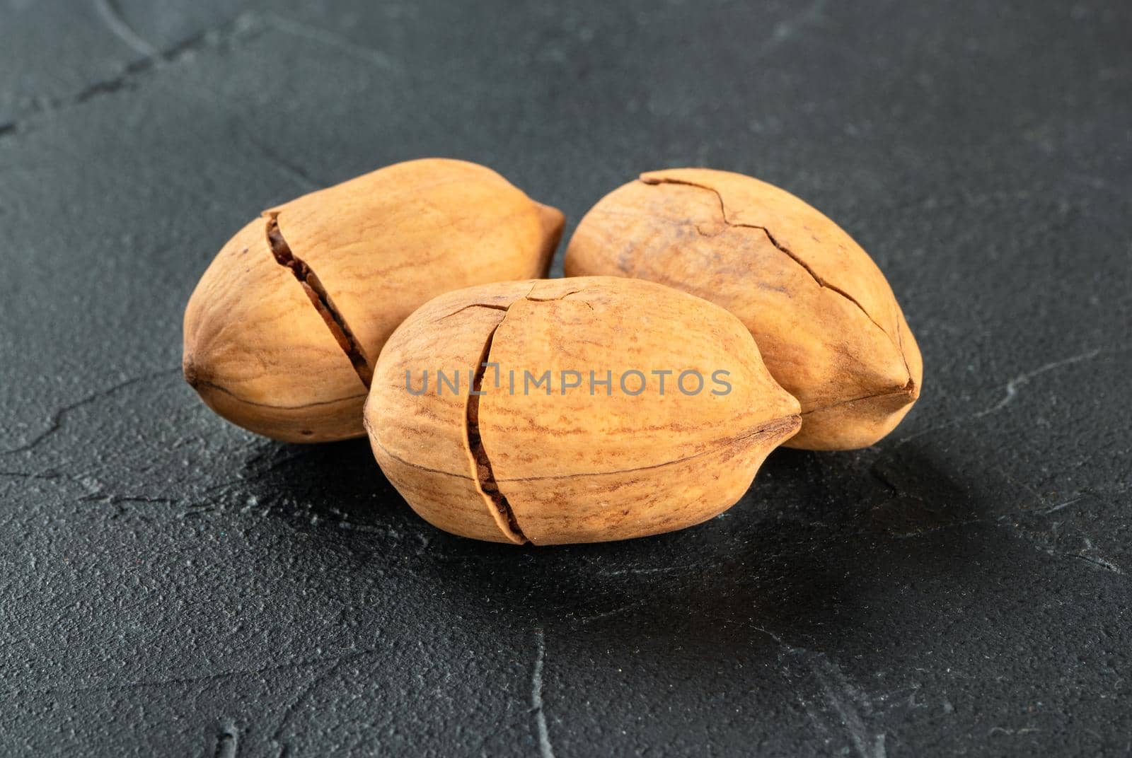 Three dry shelled pecans nuts close-up on a dark concrete background