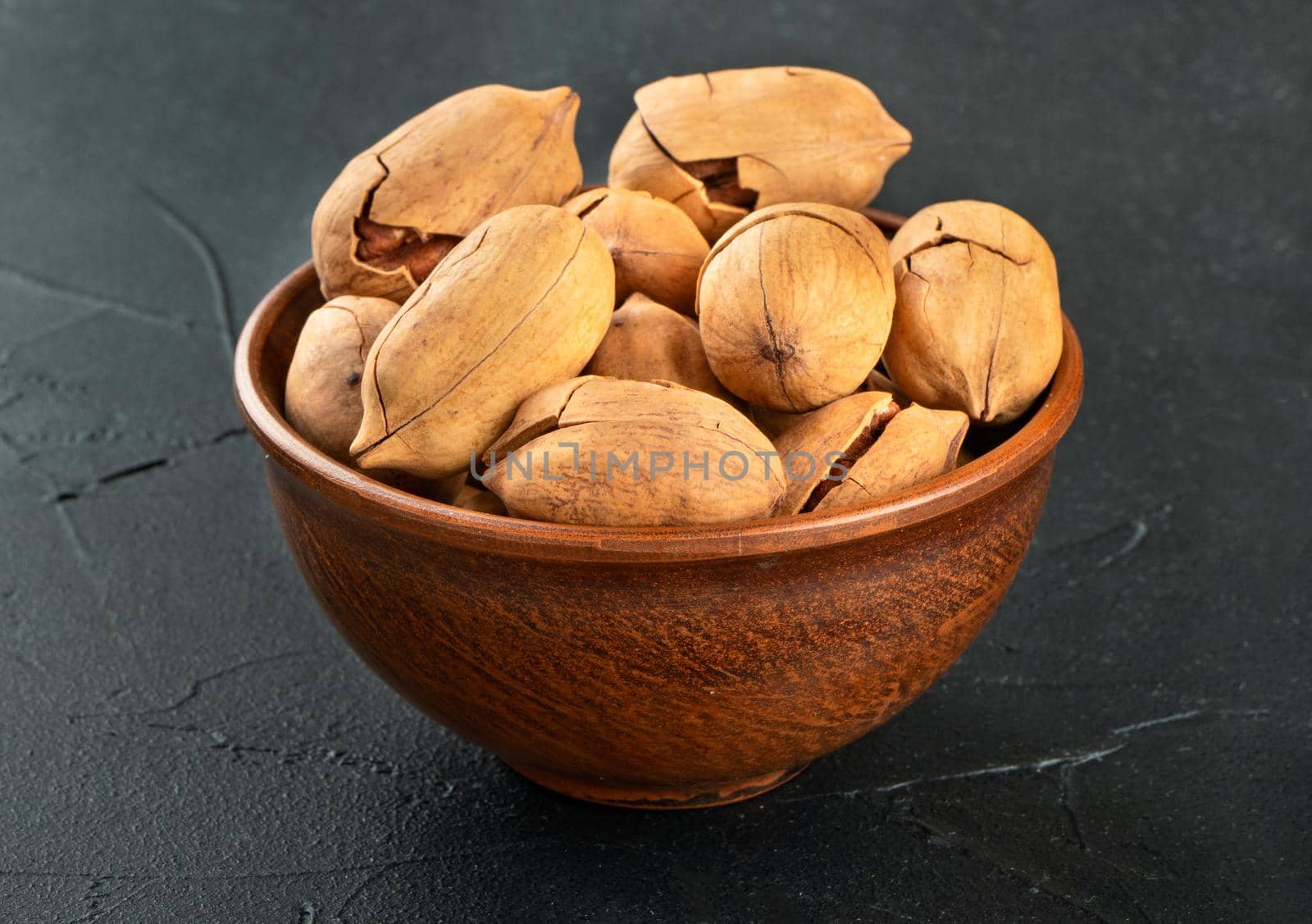 Pecan nuts in a bowl on a dark concrete background.