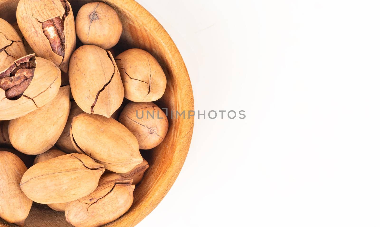 Shelled pecans in a wooden bowl close-up on an empty white background, top view