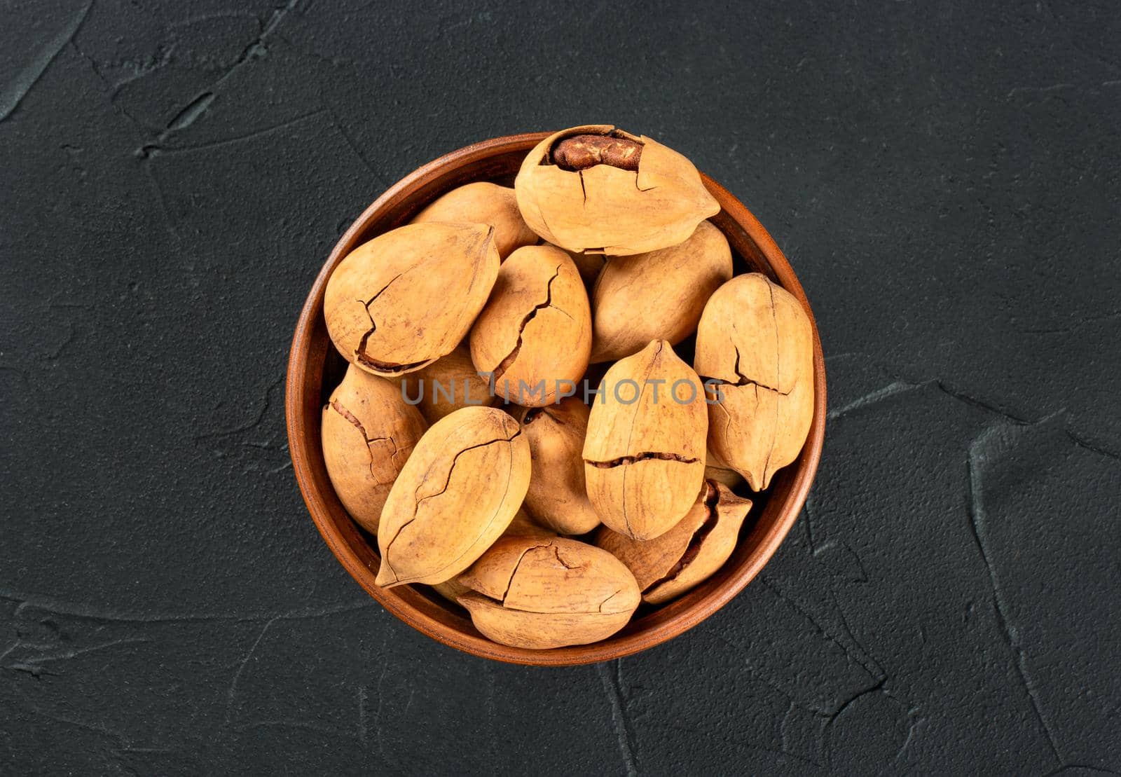 Pecan nuts in a bowl on a dark concrete background, top view.