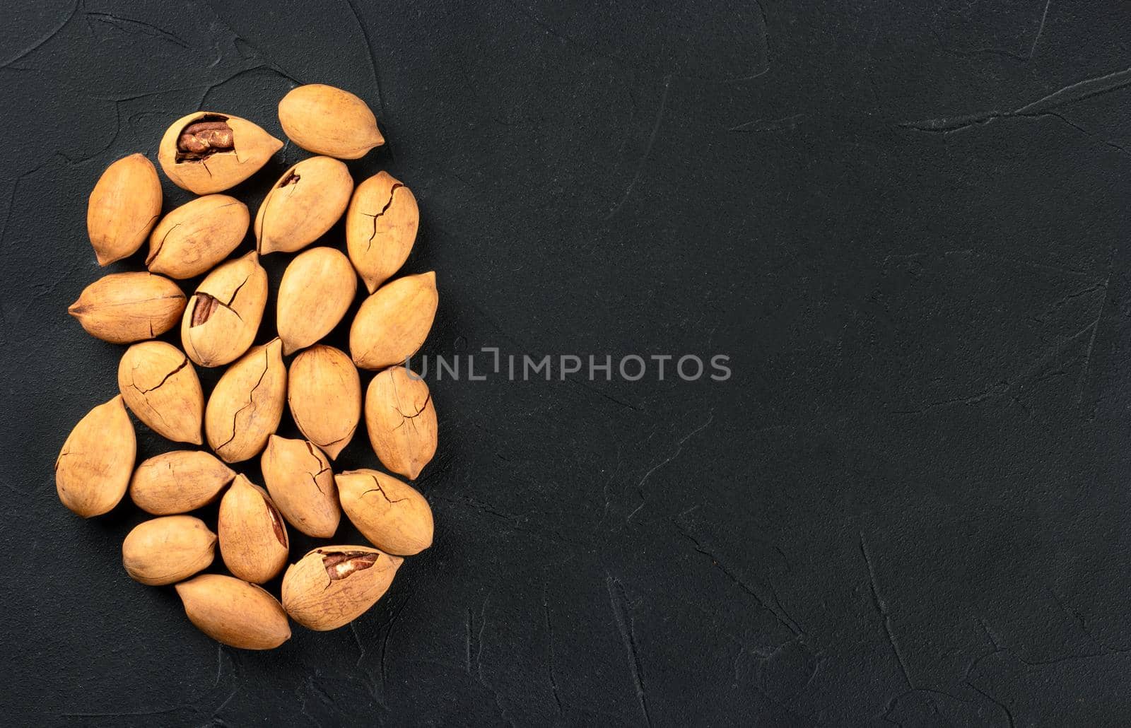 Scattered pecans in shell close up on a dark background, top view