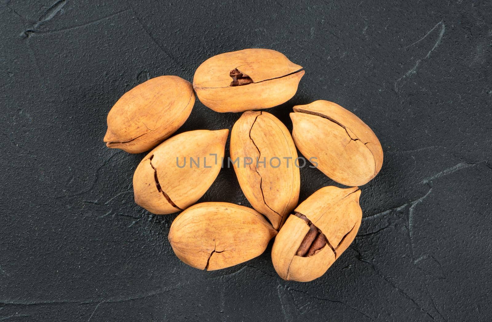 Small pile of inshell pecans on a dark background, top view
