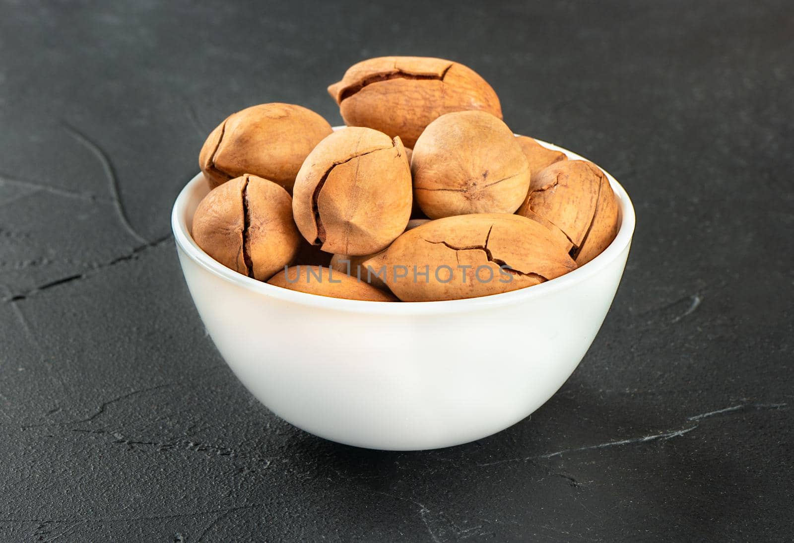 White ceramic bowl with pecans on a dark background.