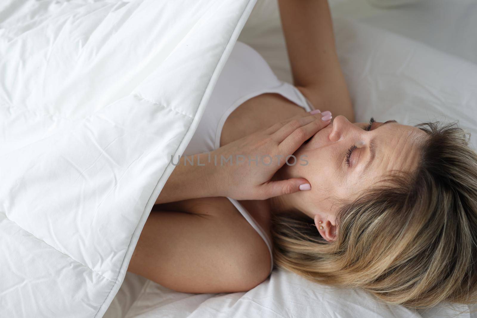 Woman looks in shock under covers in bed. Bedwetting in women concept