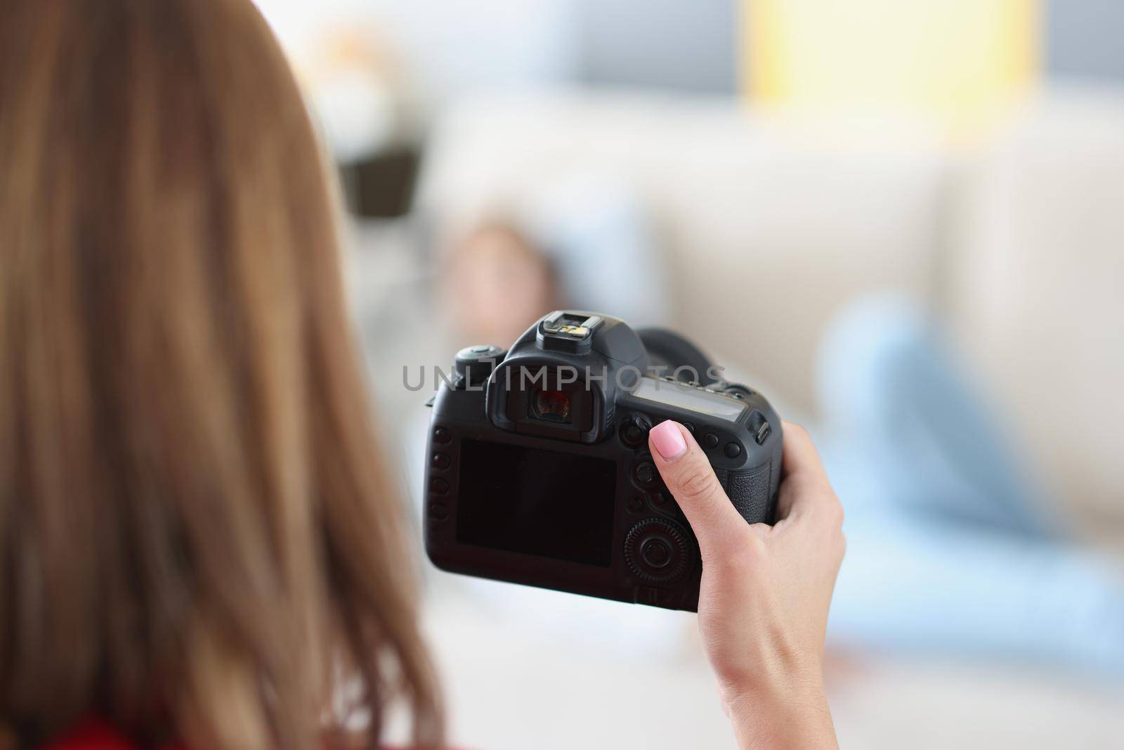 Woman holds professional black camera in hands and photographs model at home by kuprevich
