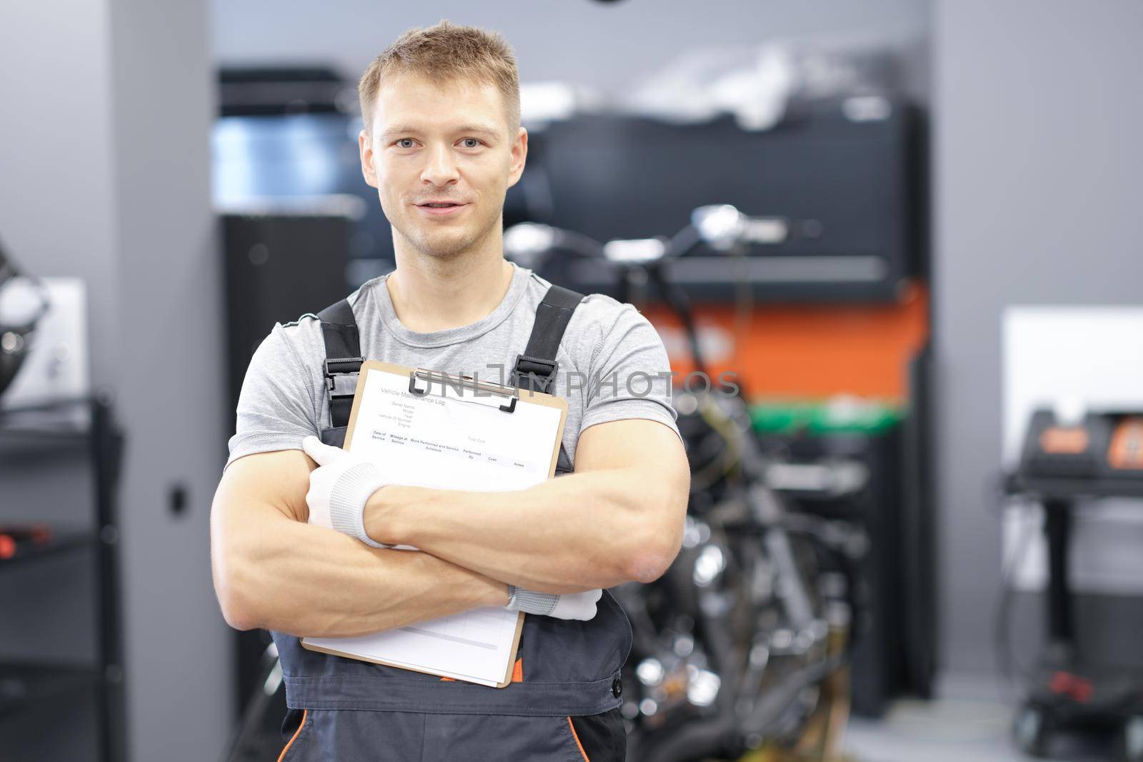 Male car mechanic holding clipboard in auto workshop. Car repair and maintenance services concept