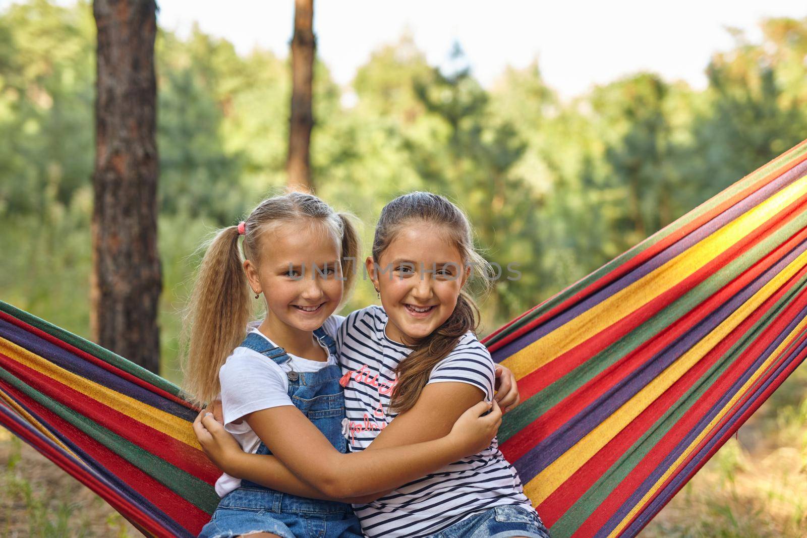 Kids relax in colorful rainbow hammock. Hot day garden outdoor fun. Afternoon nap during summer vacation. Children relaxing.