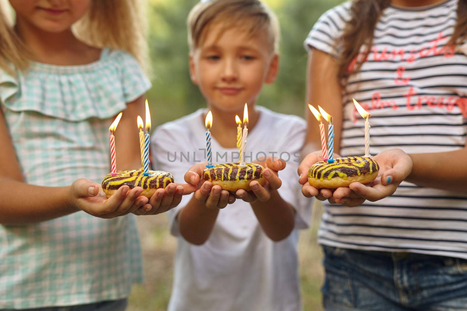 Children holding birthday cakes with burning candles. Kids party decoration and food. Boy and girls celebrating birthday in the garden with hammock. Kids with sweets.