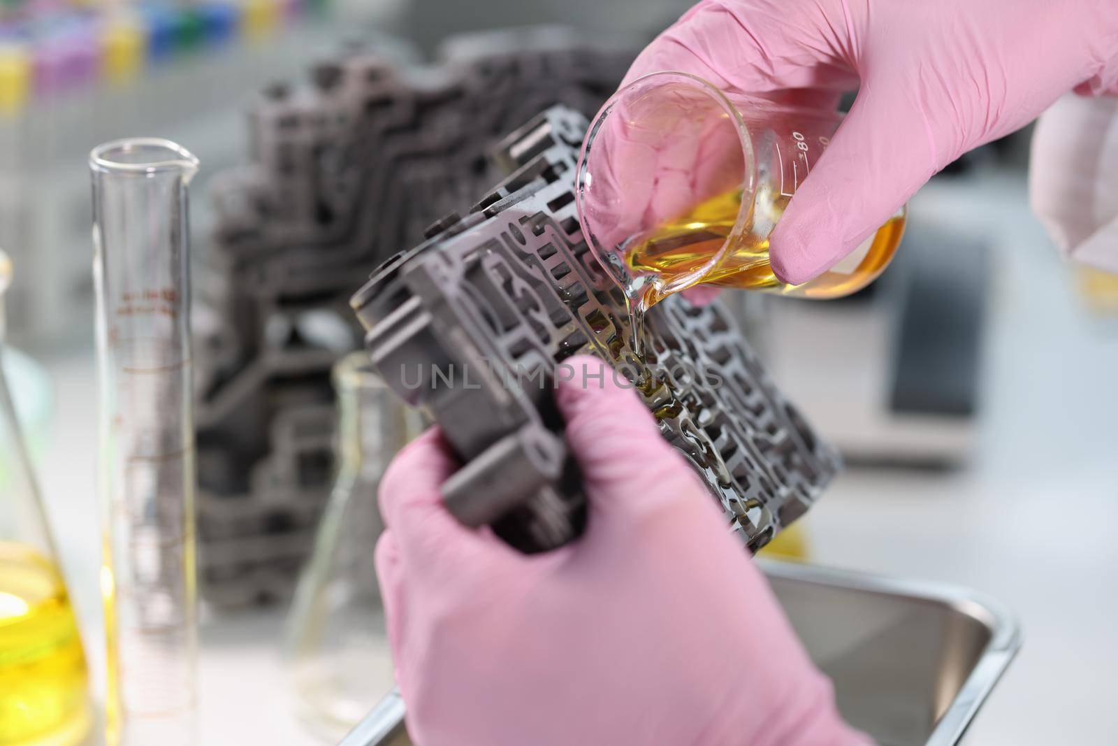 Scientist from chemical flask pours oil on gearbox valve body. Lubricants for automotive parts