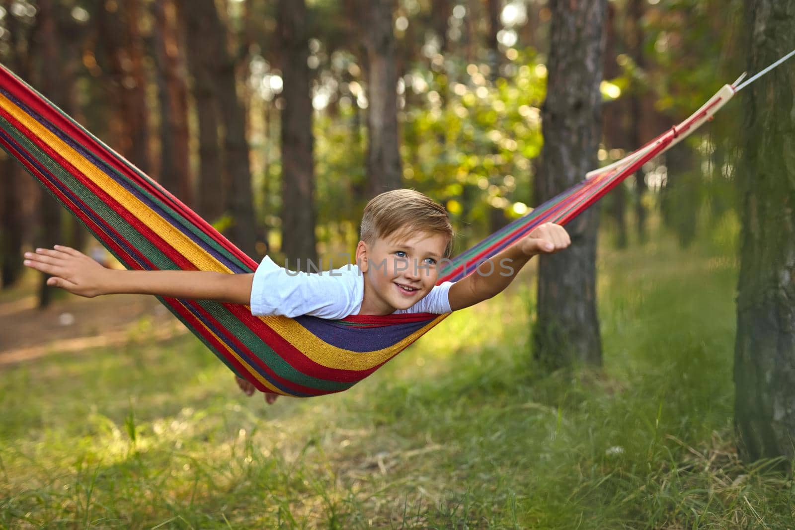 Cute boy is lying in a colorful hammock. The kid is riding in a hammock imagines himself as a flying superhero. Leisure and relax concept