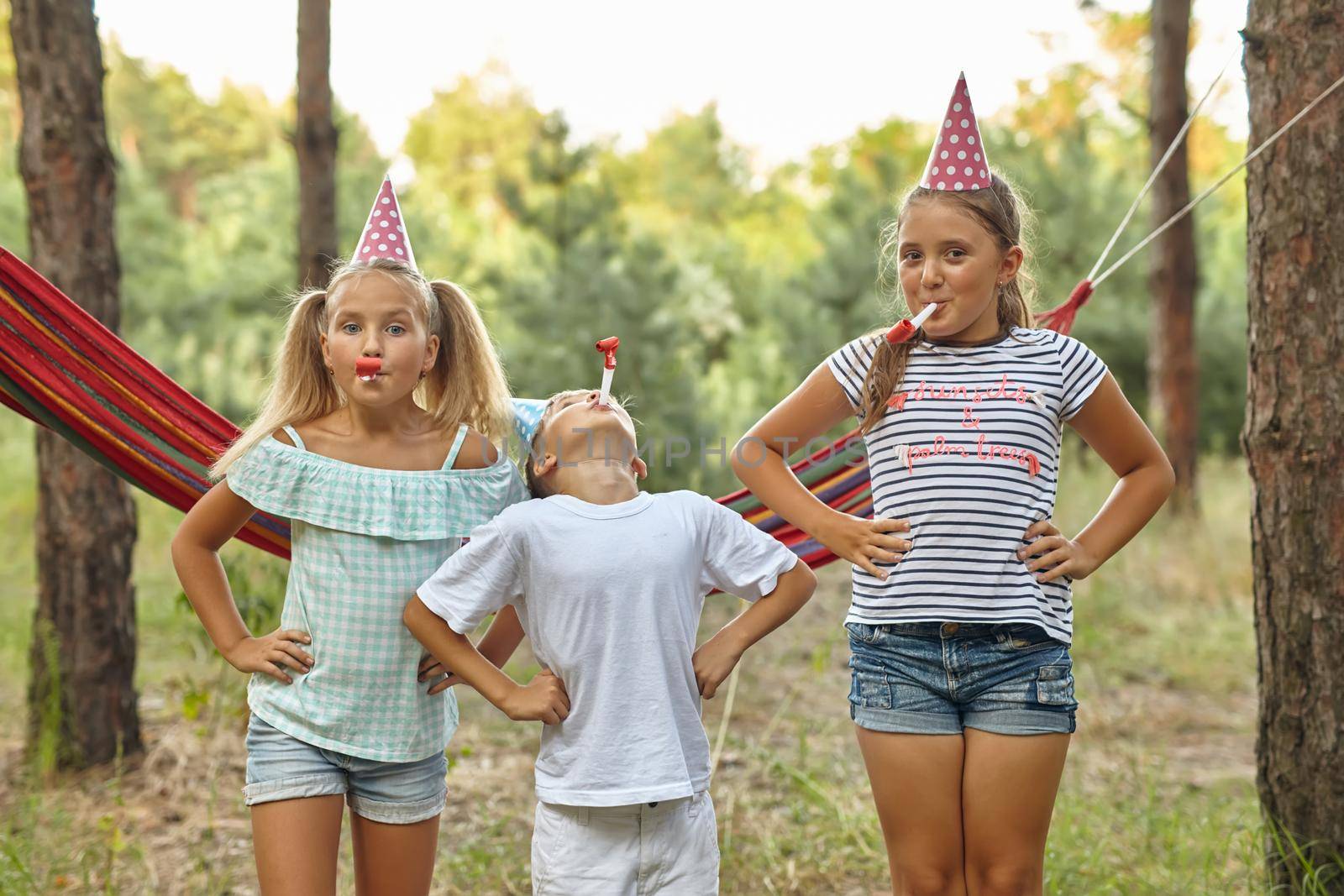 birthday, childhood and celebration concept - close up of happy kids blowing party horns and having fun in summer outdoors